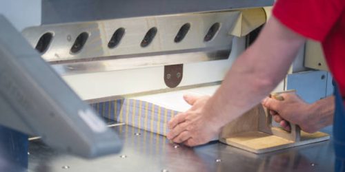 Hands of worker working on cutter guillotine machine in a printing factory, close up